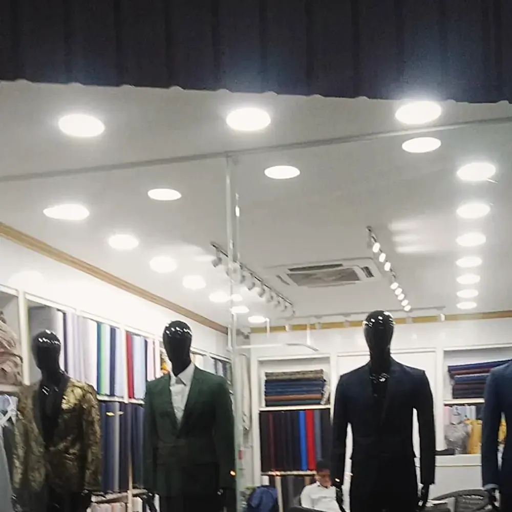 Finished suits on mannequins inside the shop — gold brocade, green check and navy — against the cloth shelves