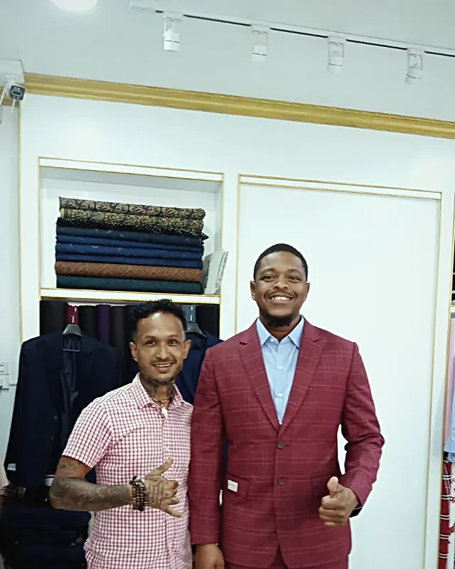 Two men in the shop, one wearing a burgundy check jacket, both smiling and giving a thumbs up